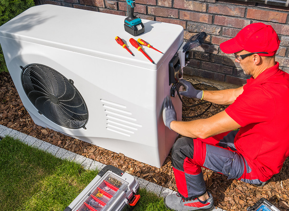 Technician installing an outdoor heat pump unit beside a residential home